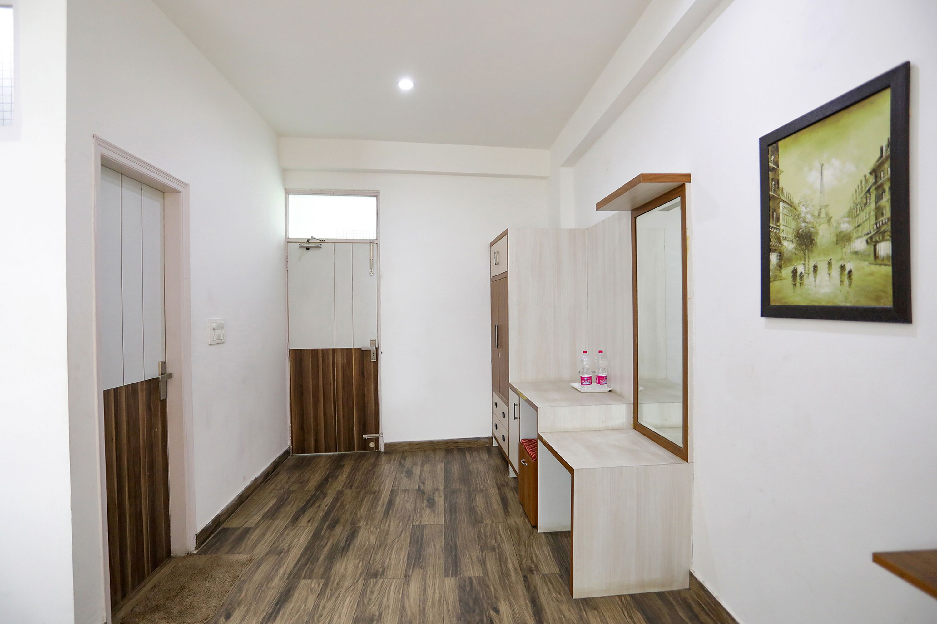 A hallway with wooden flooring, a white wall, a mirror, and a framed picture.