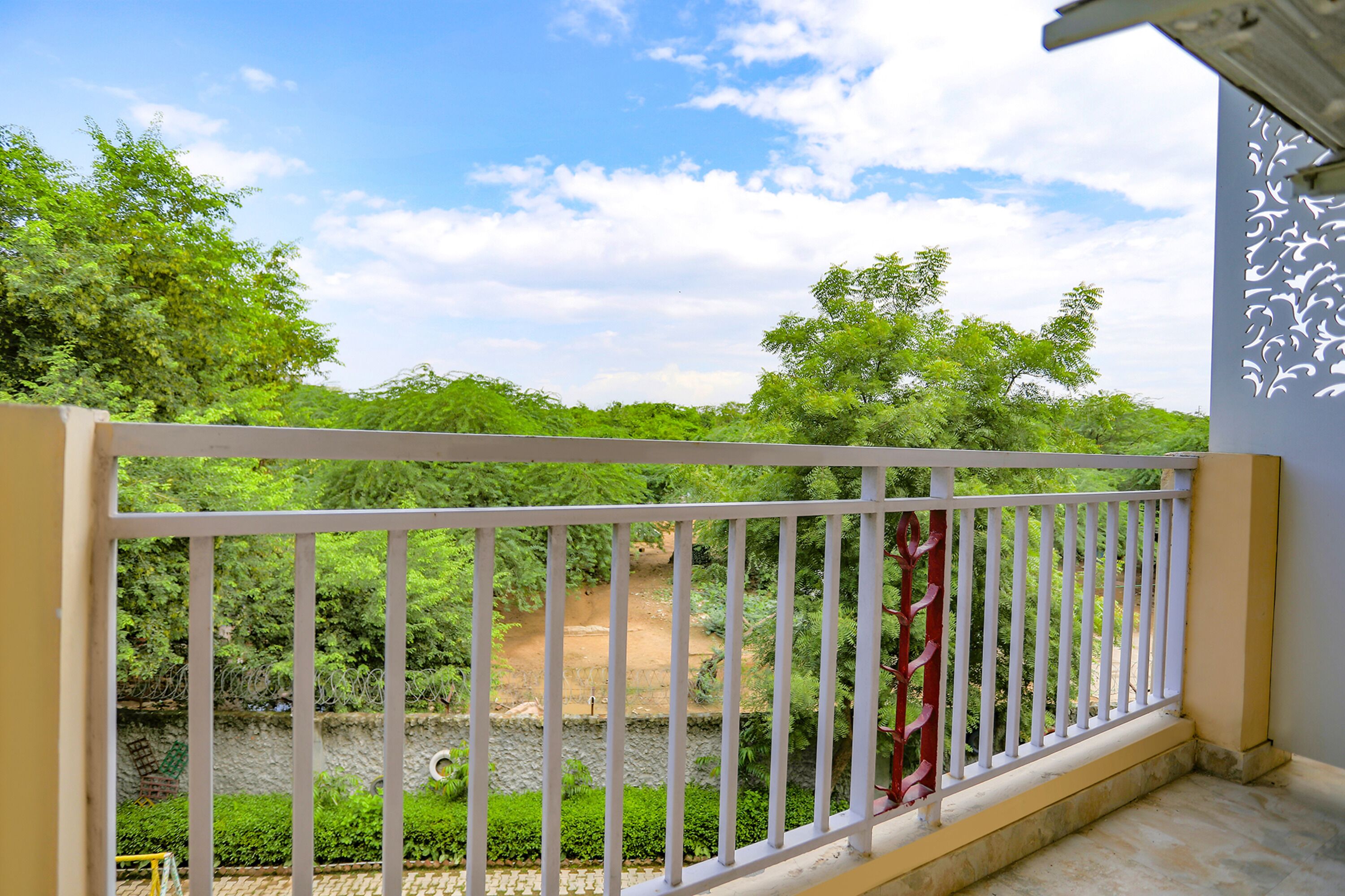 Un balcon doté d’une balustrade blanche, donnant sur un jardin où poussent différentes espèces d’arbres et où serpente un sentier.