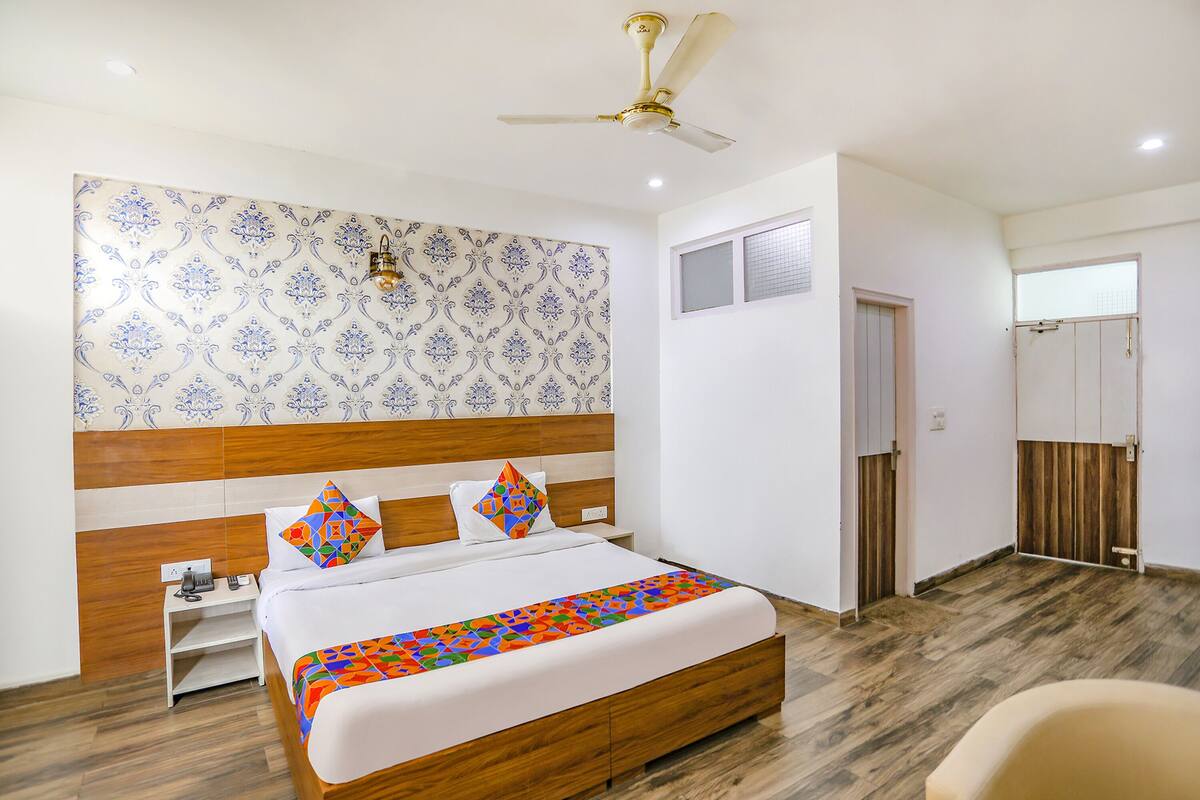 Una camera d'hotel con una testiera in legno, un letto con cuscini colorati, una ventola a soffitto e un pavimento in legno.