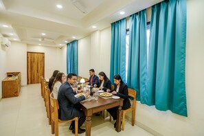 A dining area with a wooden table, teal curtains, and a wooden door. - Fabhotel Shiv Rachna (Jaipur)