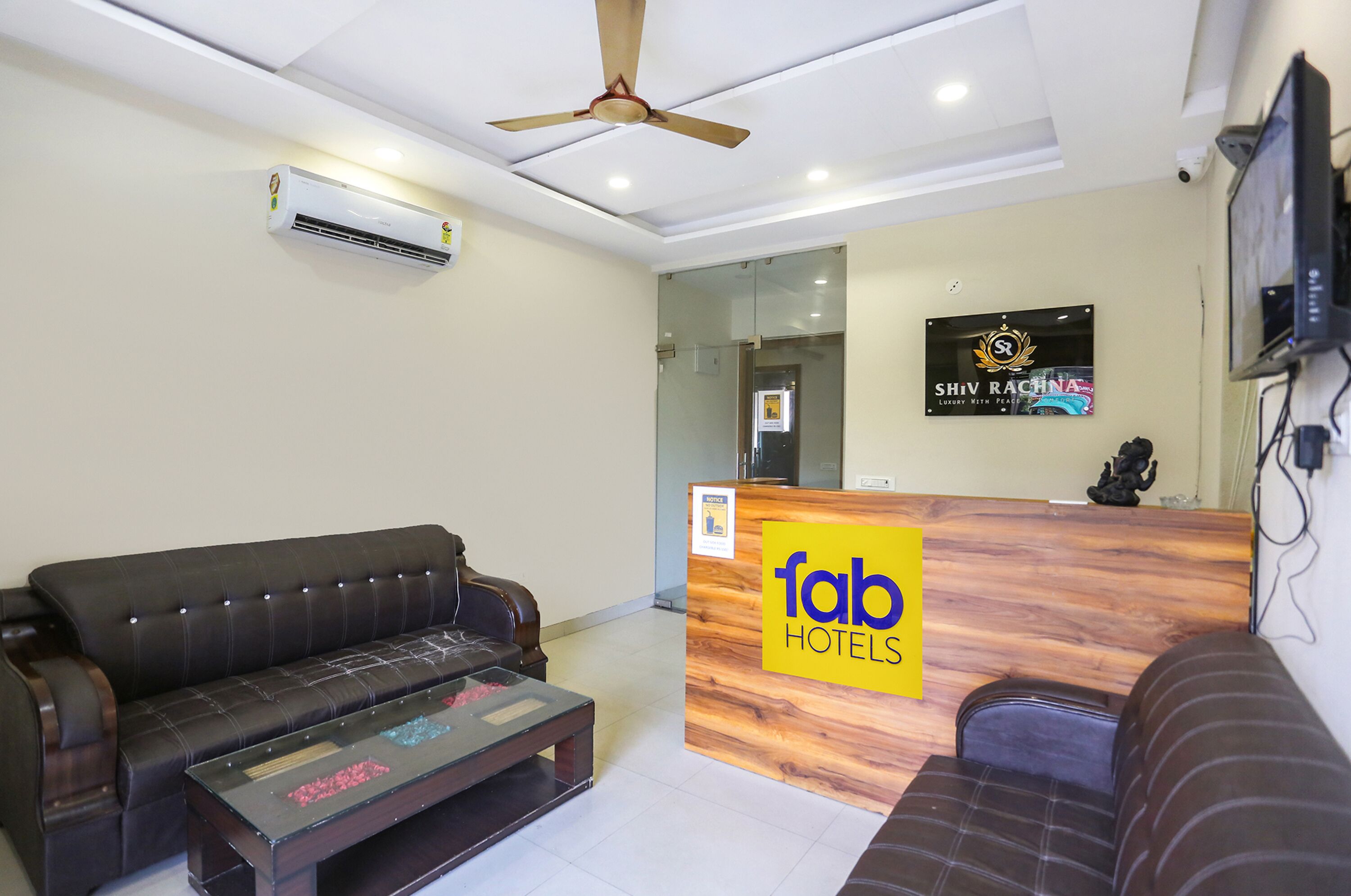 A reception area with a wooden reception desk labeled "fab hotels," a black leather sofa, a coffee table, and a ceiling fan.