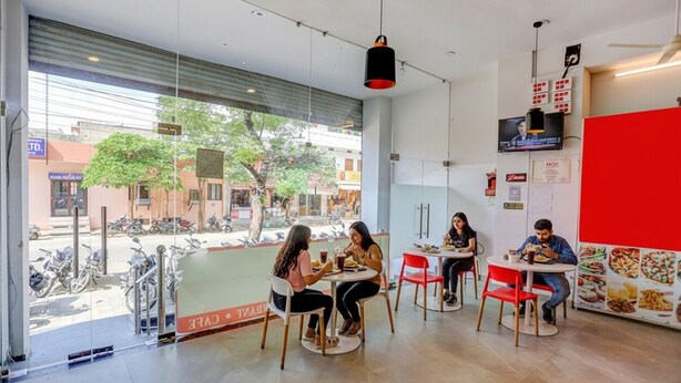 Een modern café met grote ramen, binnenzitplaatsen en een rode accentmuur.