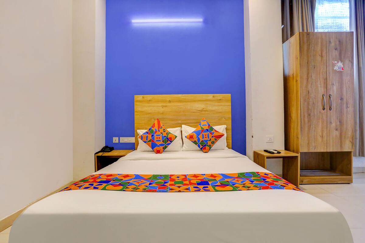 Un lit bien fait, agrémenté d’une couvre-lit aux motifs géométriques colorés, d’une tête de lit en bois et de deux coussins décoratifs.