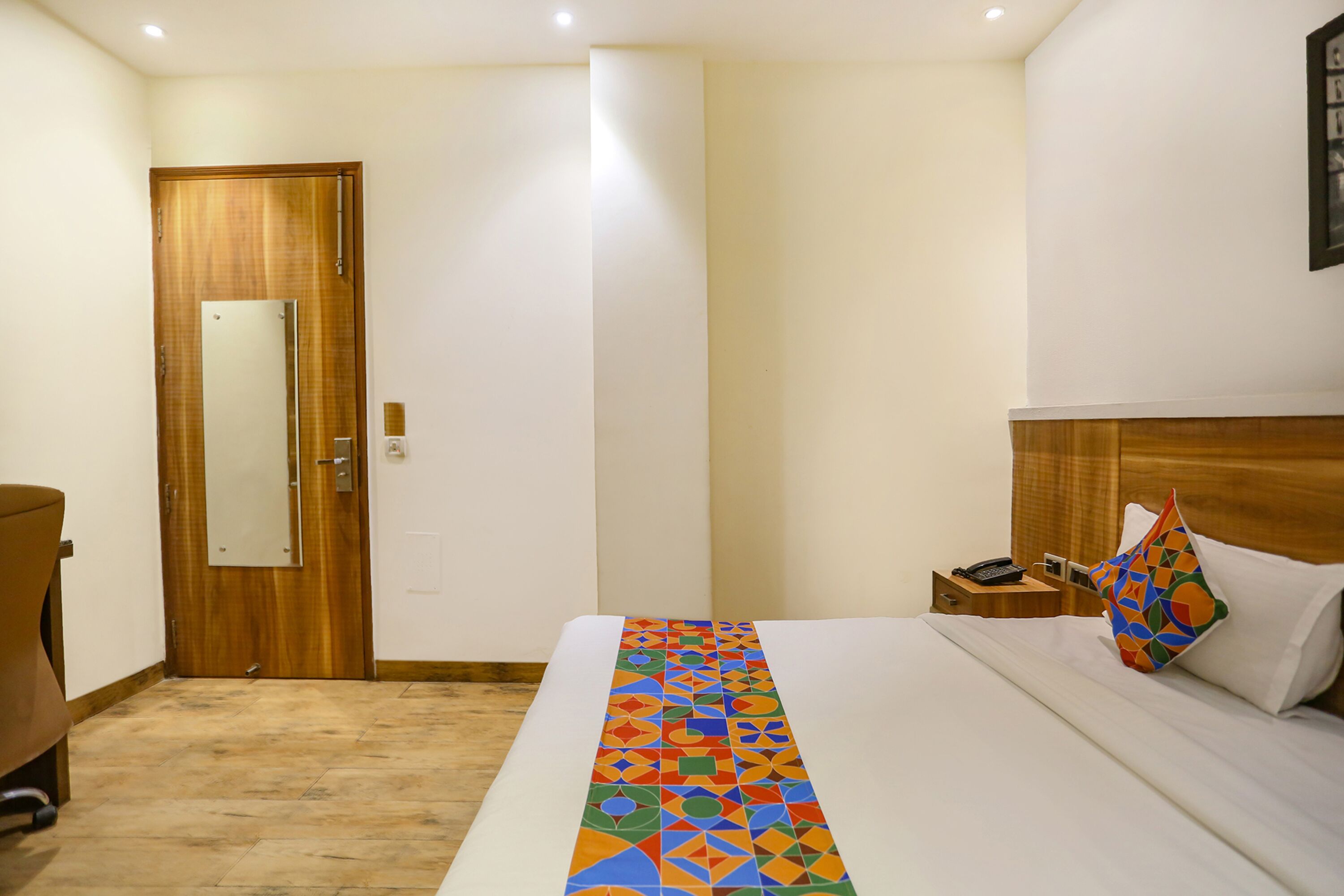 Een hotelkamer met een bed, een nachtkastje, een houten deur en een spiegel.