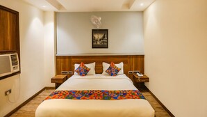 A hotel room with a large bed, a wooden headboard, two bedside tables with lamps, a wall-mounted air conditioner, and a framed picture above the bed. - Fabhotel Royal Touch (New Delhi)