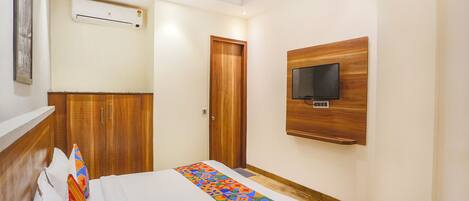 A hotel room with a bed, a TV mounted on the wall, and a wooden wardrobe.