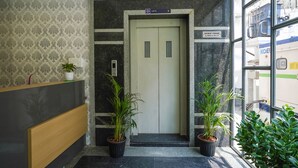Un ascenseur avec un panneau indiquant « ascenseur », un comptoir d’accueil et des plantes en pot.