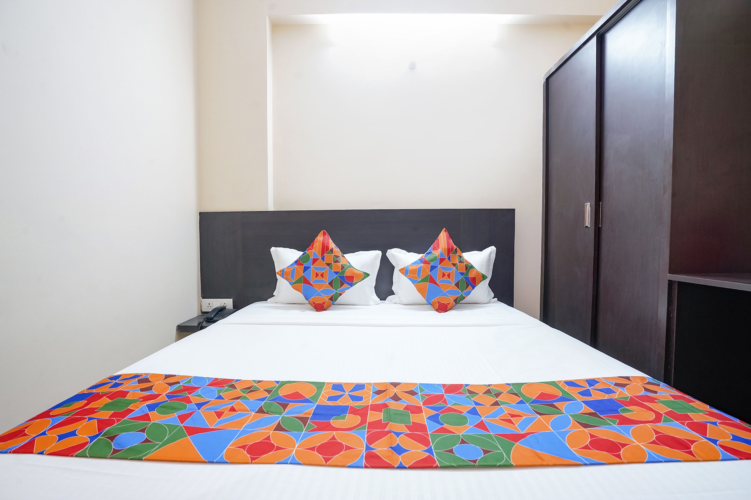 Una habitación de hotel con una cama, dos almohadas, una mesita de noche y un armario.
