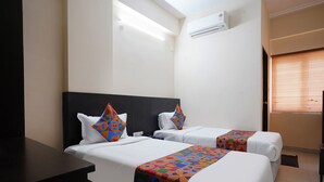 Une chambre d’hôtel avec deux lits, une tête de lit sombre, une grande fenêtre avec des stores et un climatiseur fixé au mur.