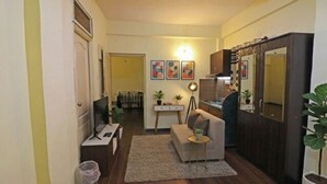 A compact living space with a sofa, a small table, a desk with a computer, a kitchen area, and a dining table. - FabHotel East Field Homes (Pune)