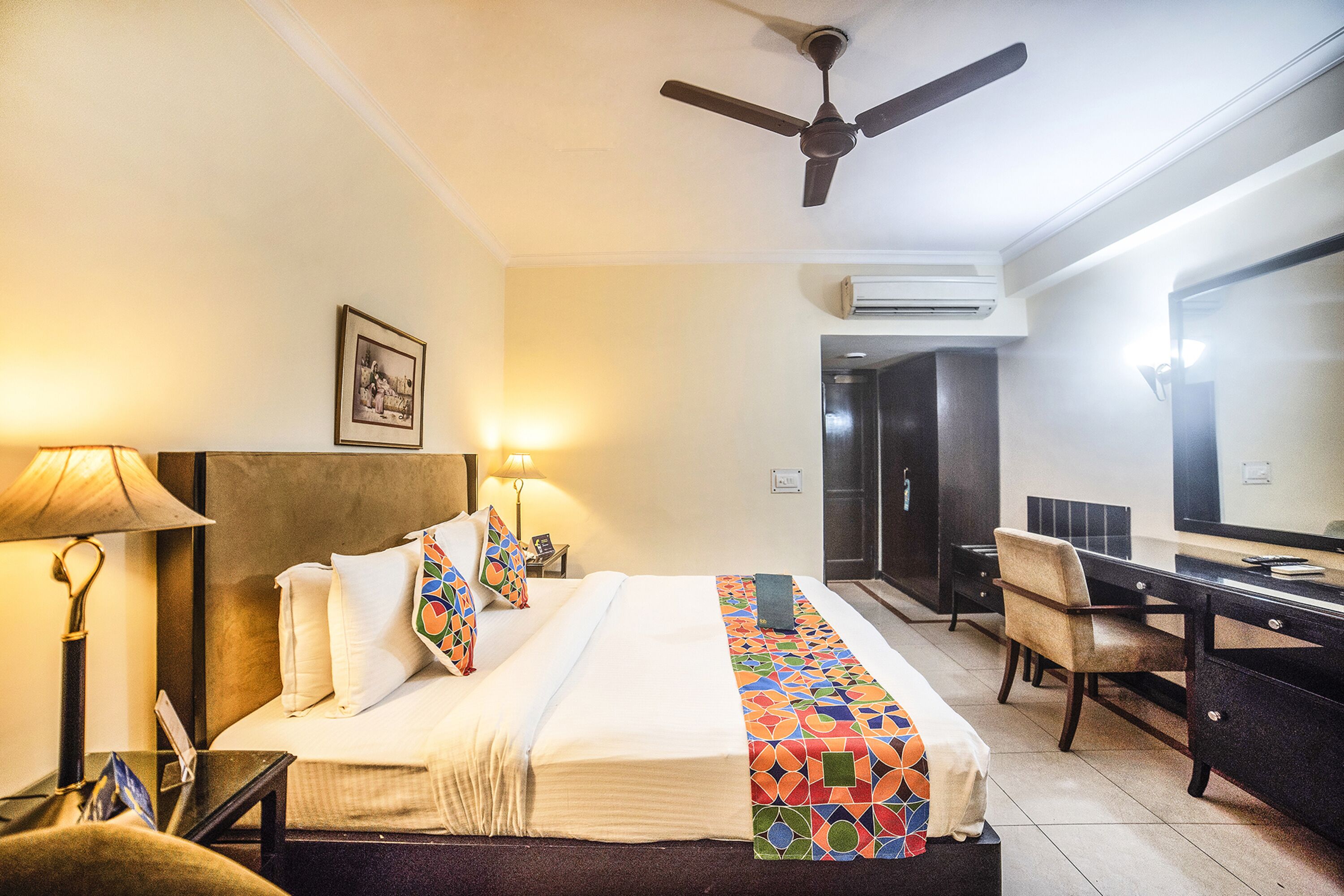 A hotel room with a bed, desk, chair, lamp, and ceiling fan.