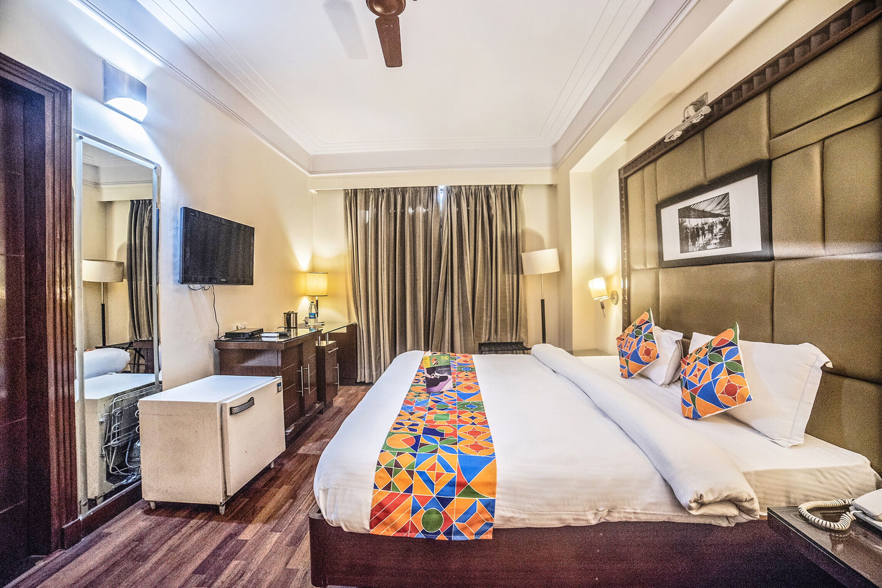 Una habitación de hotel con una cama grande, un escritorio, una silla, un televisor y un espejo.