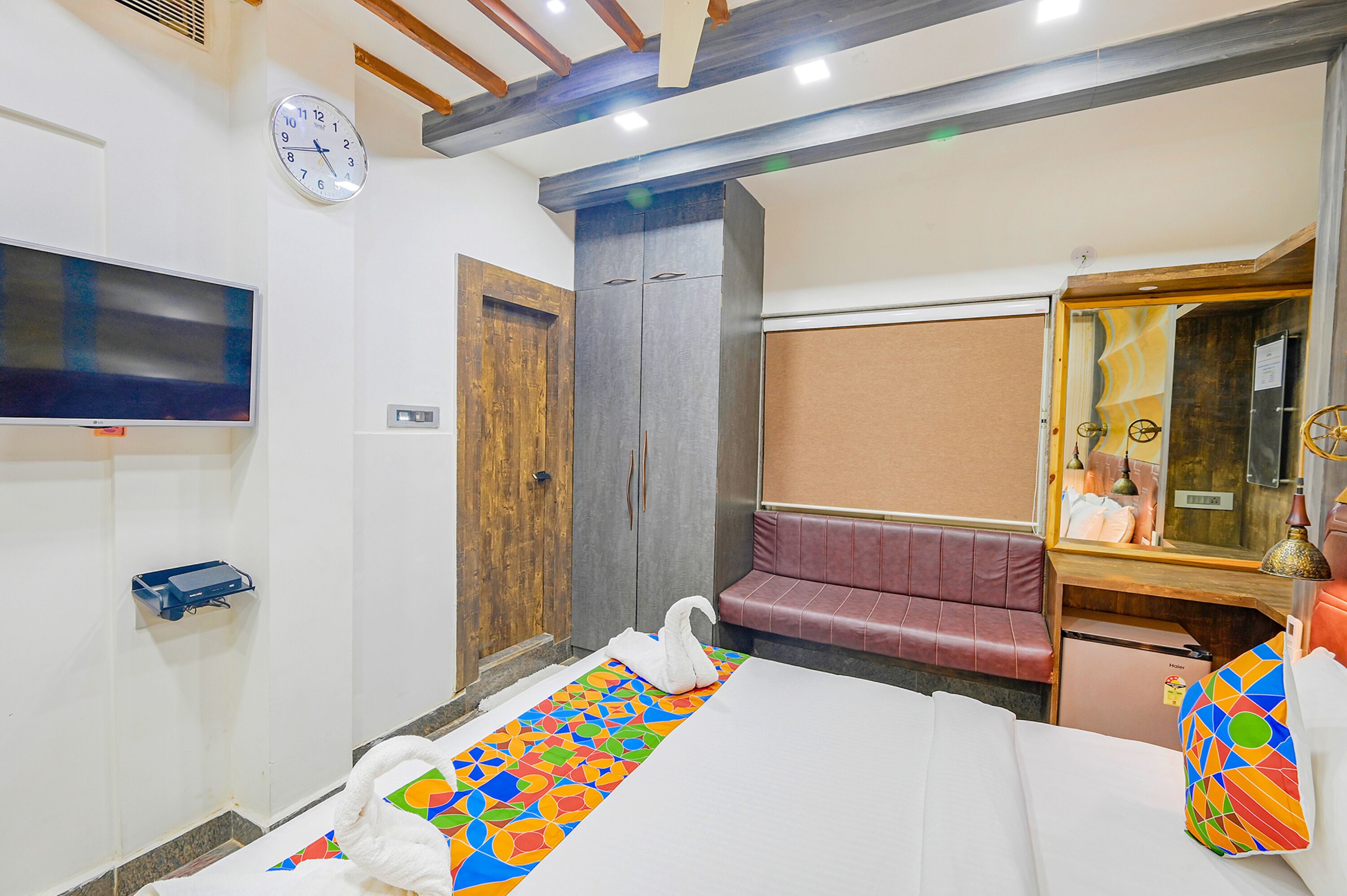 A hotel room with a bed, a TV, a wardrobe, a seating area, and a mirror.