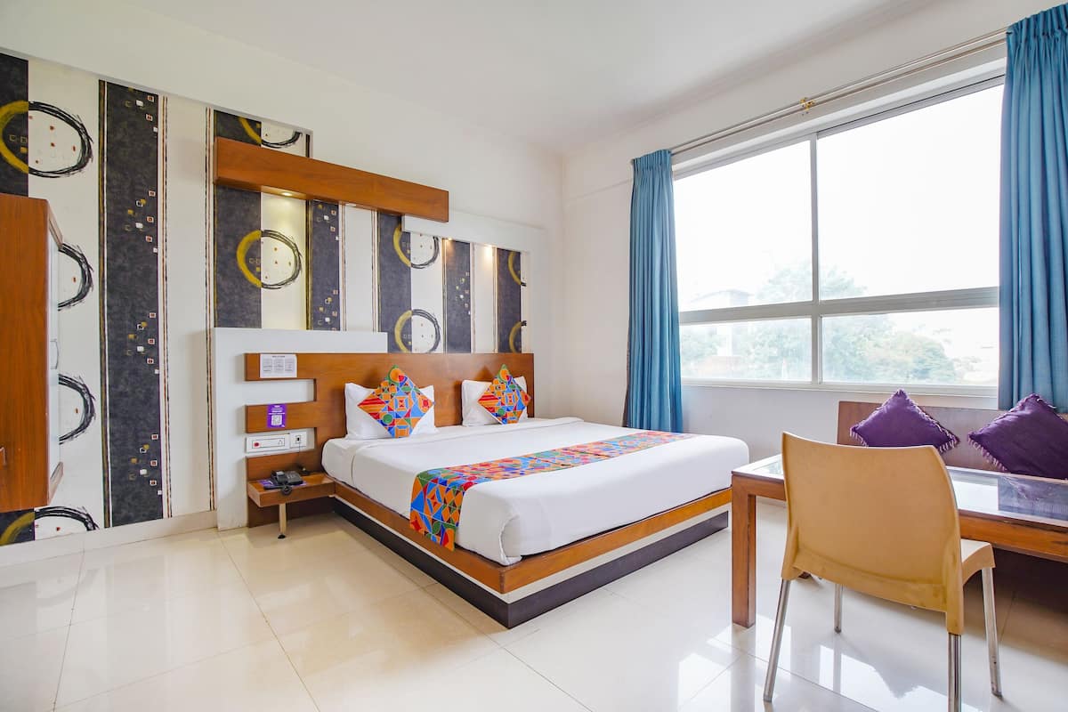A hotel room with a bed, a desk, a chair, a nightstand, and a wall with a clock design.