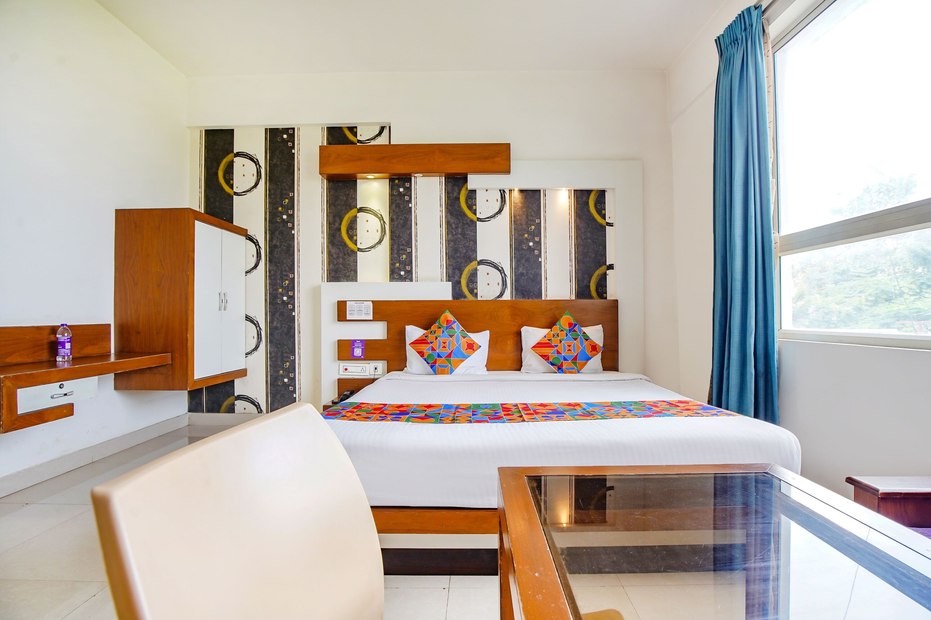 Ein Hotelzimmer mit Bett, Schreibtisch, Stuhl und einem fenster mit Vorhängen.