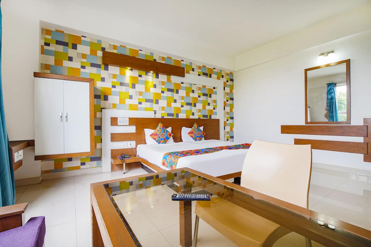 A hotel room with a bed, a desk, a chair, a wardrobe, and a colorful mosaic wall.