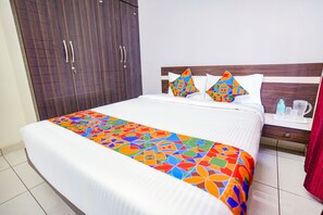 Habitación de hotel con una cama grande, un armario de madera y una mesita de noche con una botella de agua y una taza.