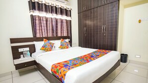 Una habitación de hotel con una cama grande, una mesita de noche, un armario y una ventana con cortinas.