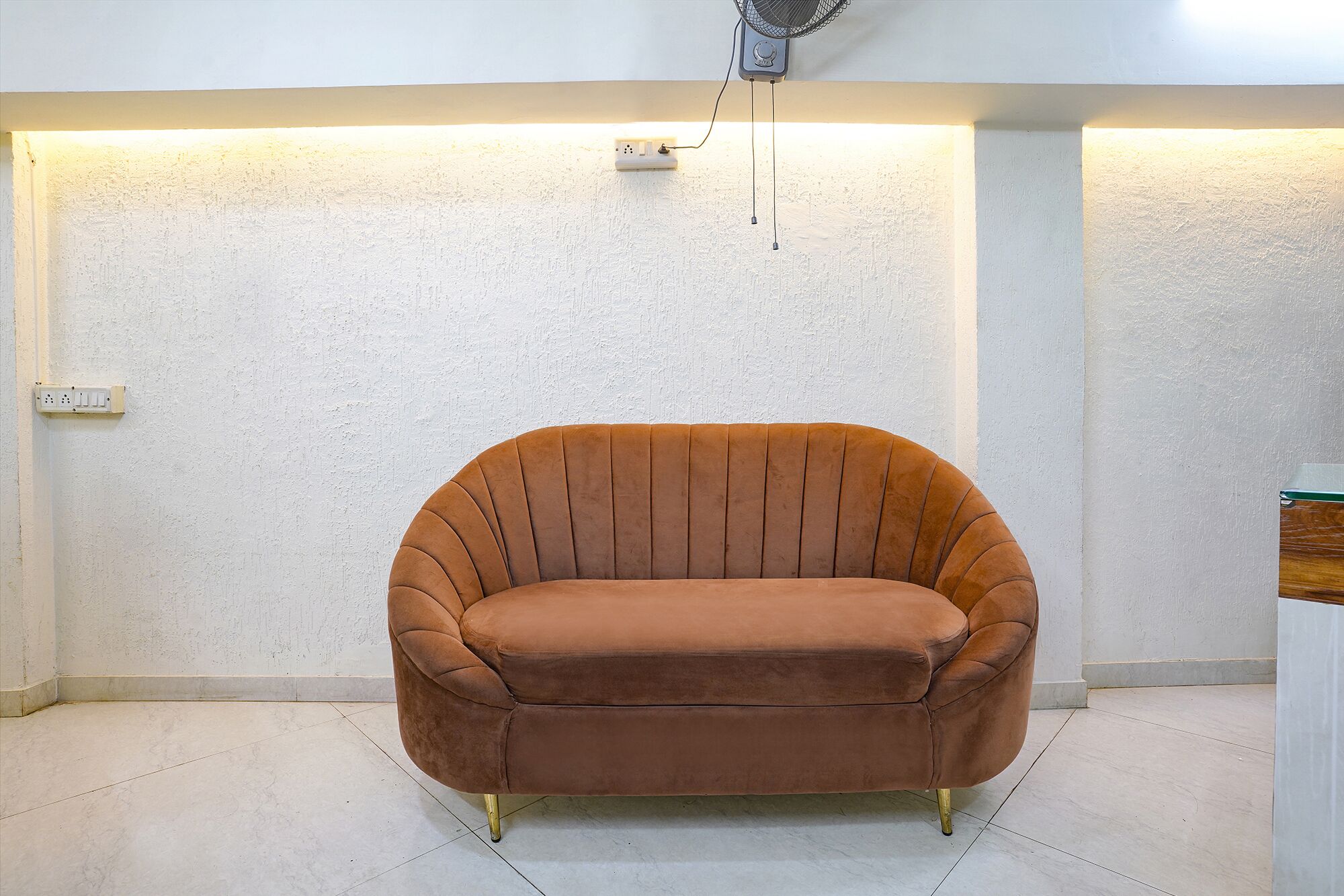 Une pièce avec un fauteuil à revêtement marron, un mur blanc à texture et un interrupteur.
