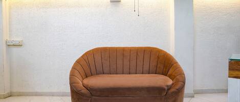 Une pièce avec un fauteuil à revêtement marron, un mur blanc à texture et un interrupteur.