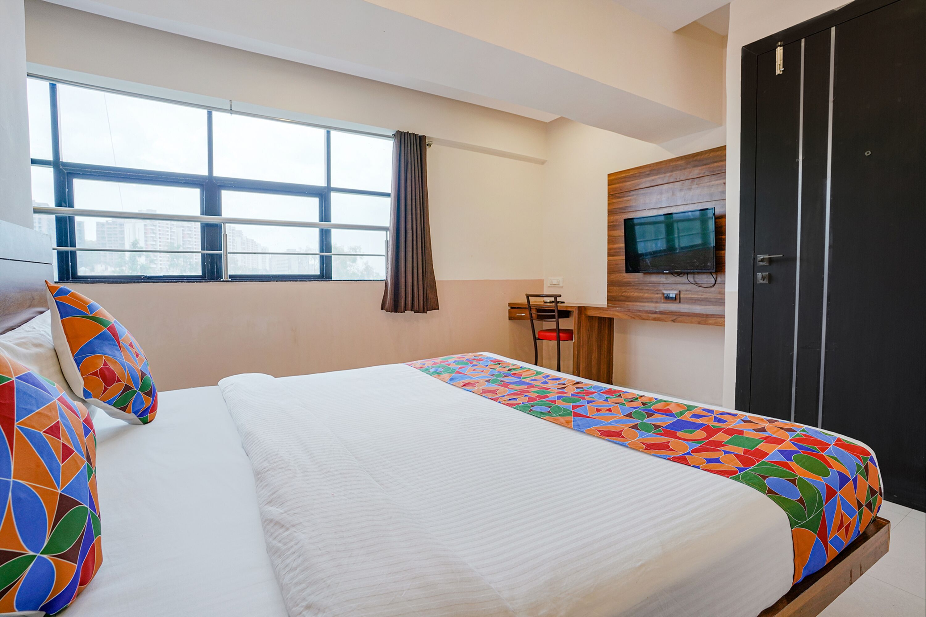 Habitació d'hotel amb un llit, una televisió penjada a la paret, escriptori amb cadira i un armari gran.
