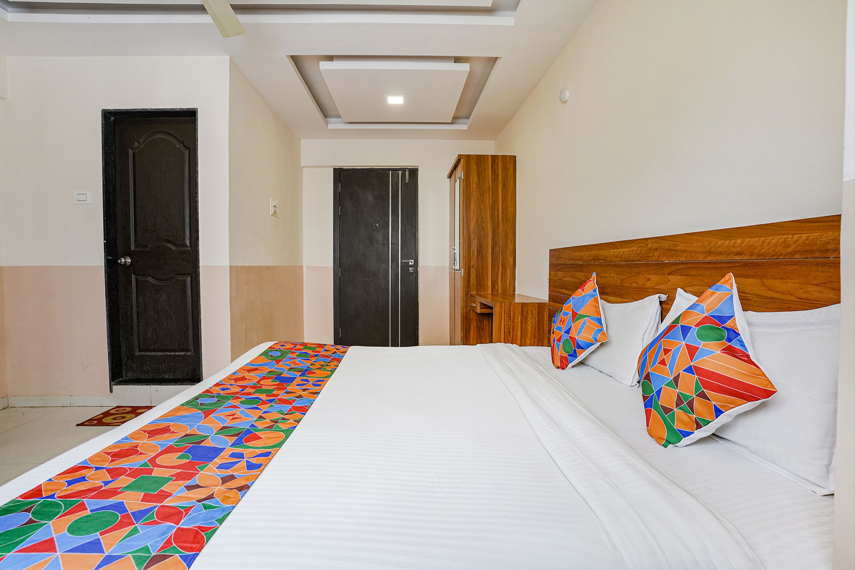 A hotel room with a large bed, a wooden headboard, and a colorful geometric runner.