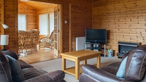 L’intérieur d’un chalet confortable, avec un plancher en bois, des canapés en cuir, une table basse en bois, un téléviseur et une cheminée.