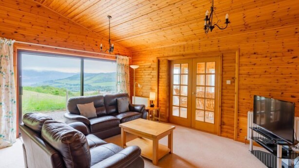 L’intérieur d’un chalet chaleureux, avec un canapé en cuir, une table basse en bois et un téléviseur.