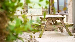 Une table et des chaises en bois, installées sur une terrasse, avec un mur en pierre et une vue sur un paysage verdoyant.
