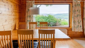 Un intérieur en bois avec une table et des chaises, une fenêtre avec des rideaux et une lampe.