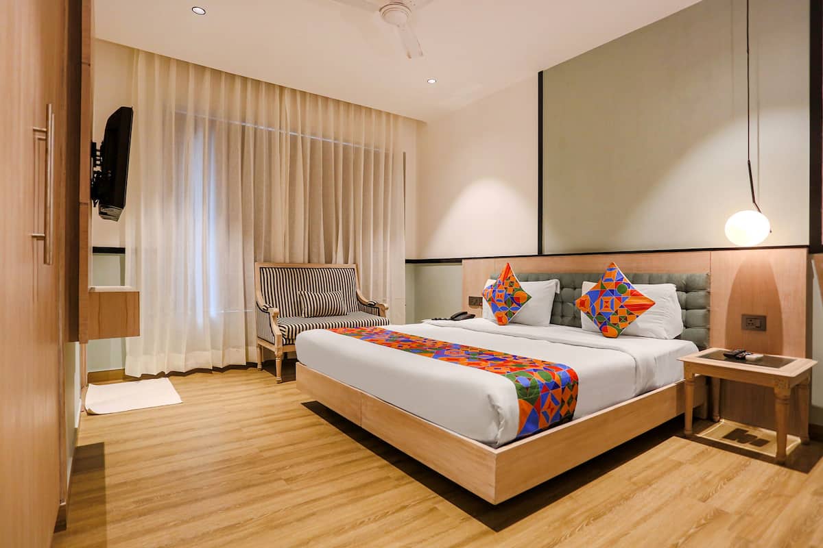 A modern hotel room with a large bed, a chair, a bedside table, and a large mirror.