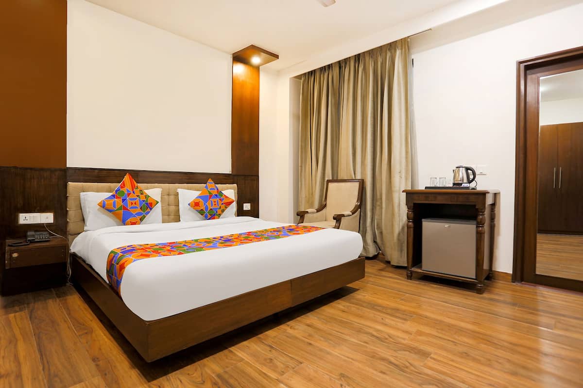 A hotel room with a large bed, a nightstand, a desk with a kettle, and a wardrobe.