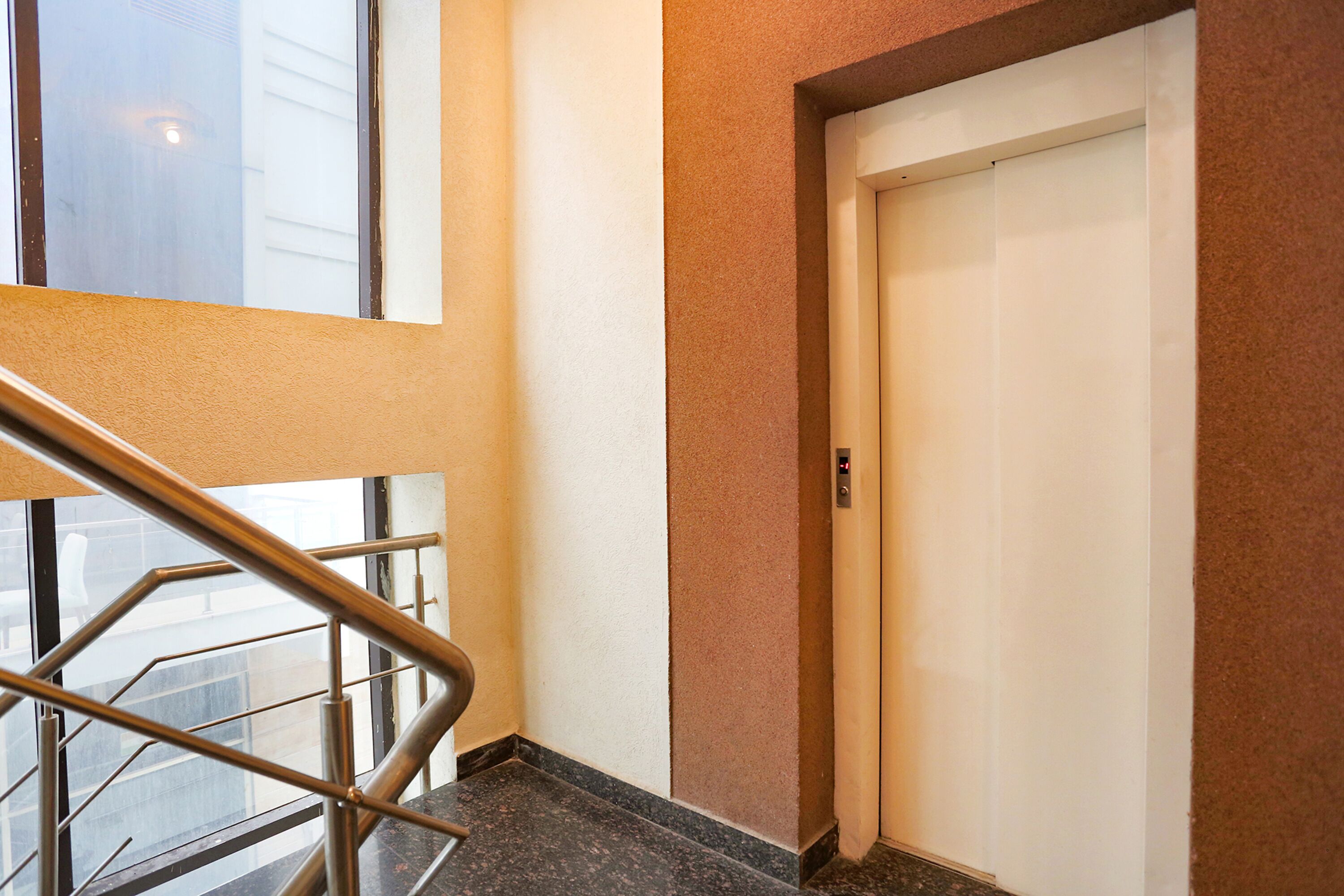 A modern elevator with a control panel, a metal handrail, and a door.