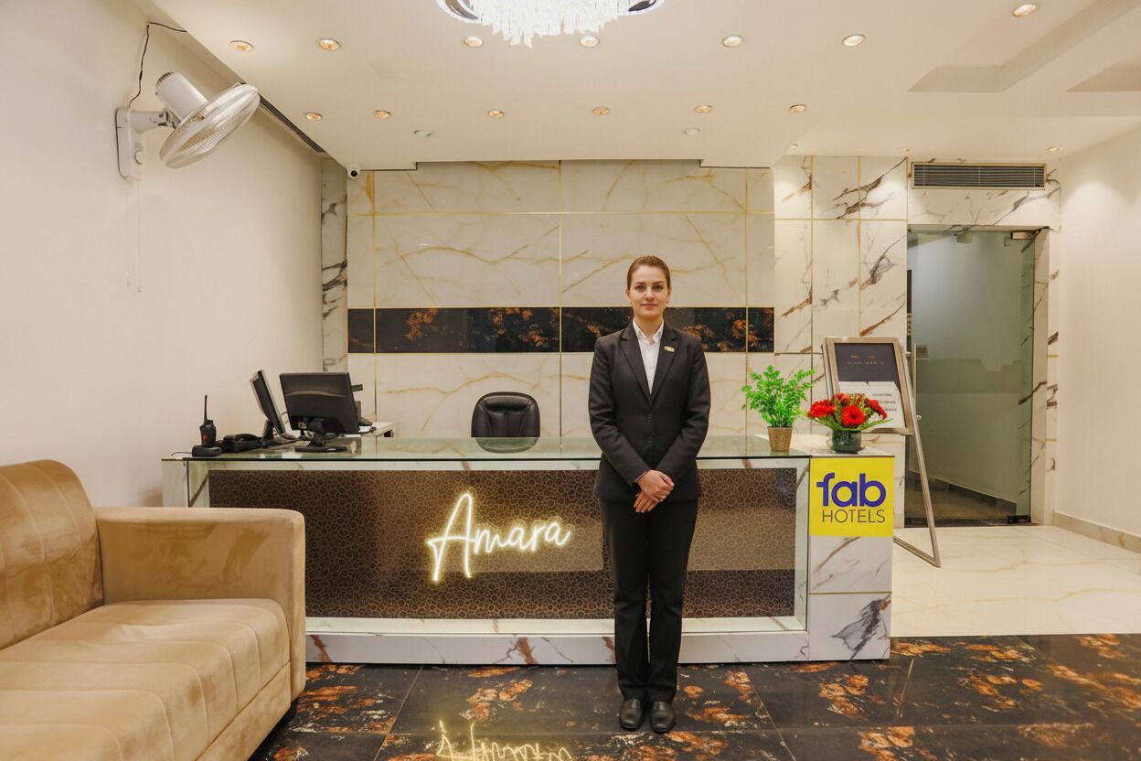 A hotel reception area with a marble reception desk, a sofa, a fan, and a sign for 'Fab Hotels'.