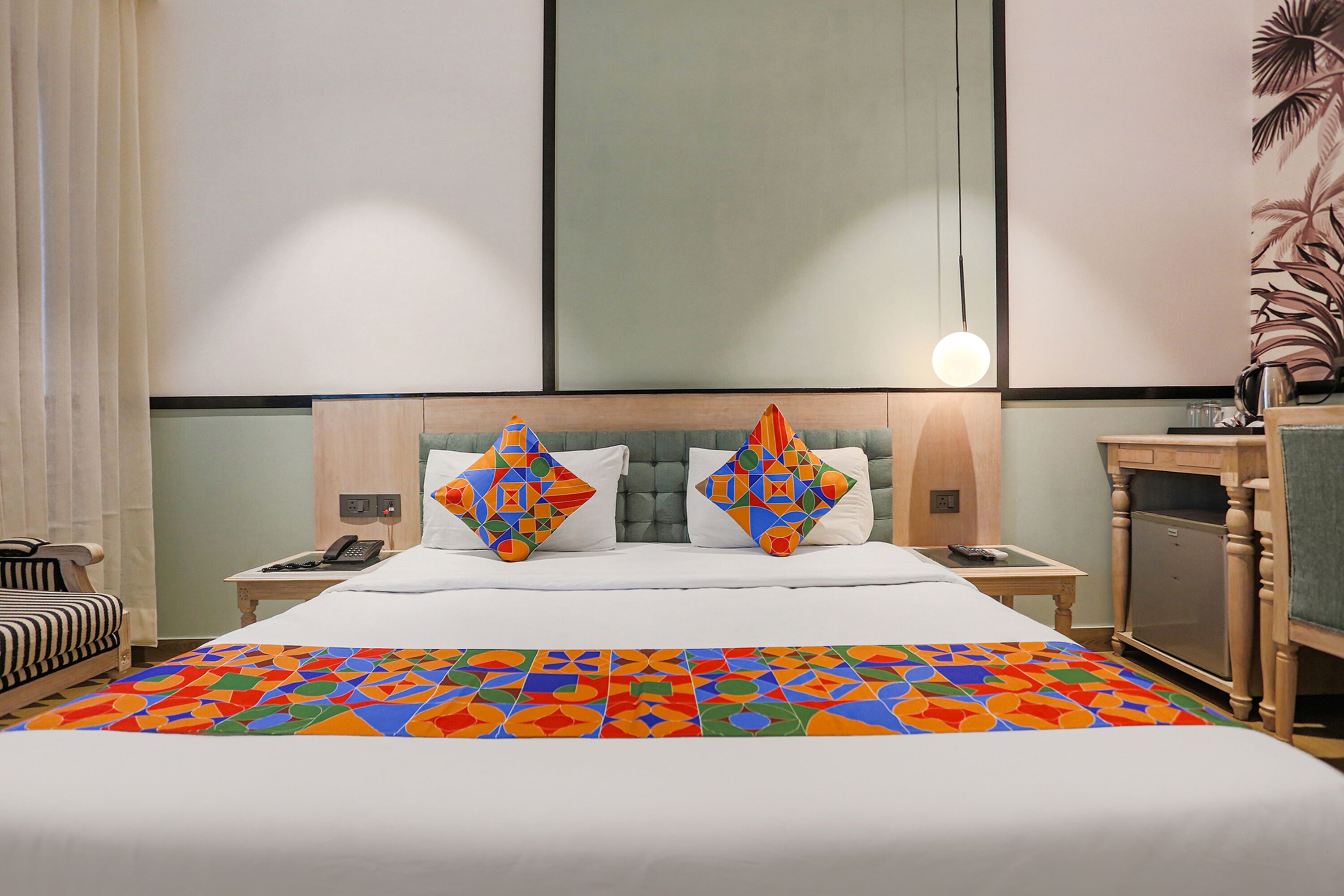 Habitación de hotel con una cama grande, dos almohadas decorativas, una mesita de noche con un teléfono, una lámpara y un pequeño armario.