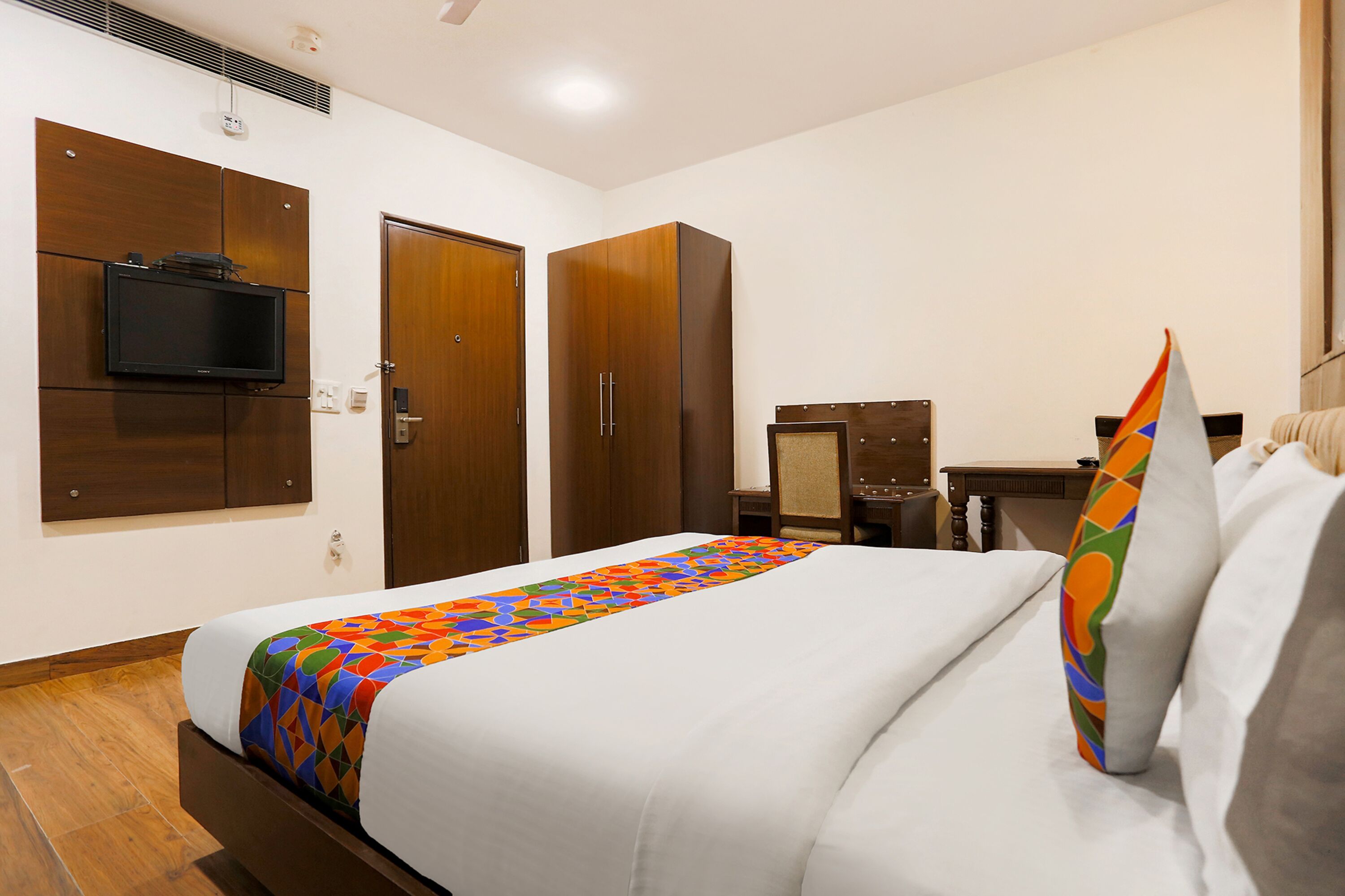 Een hotelkamer met een bed, een aan de muur bevestigde televisie, een kledingkast en een bureau met een stoel.