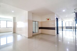 A spacious, well-lit hallway with a tiled floor, a window with metal bars, and a fire alarm on the wall. - Fabhotel Champion Residency (Bengaluru)