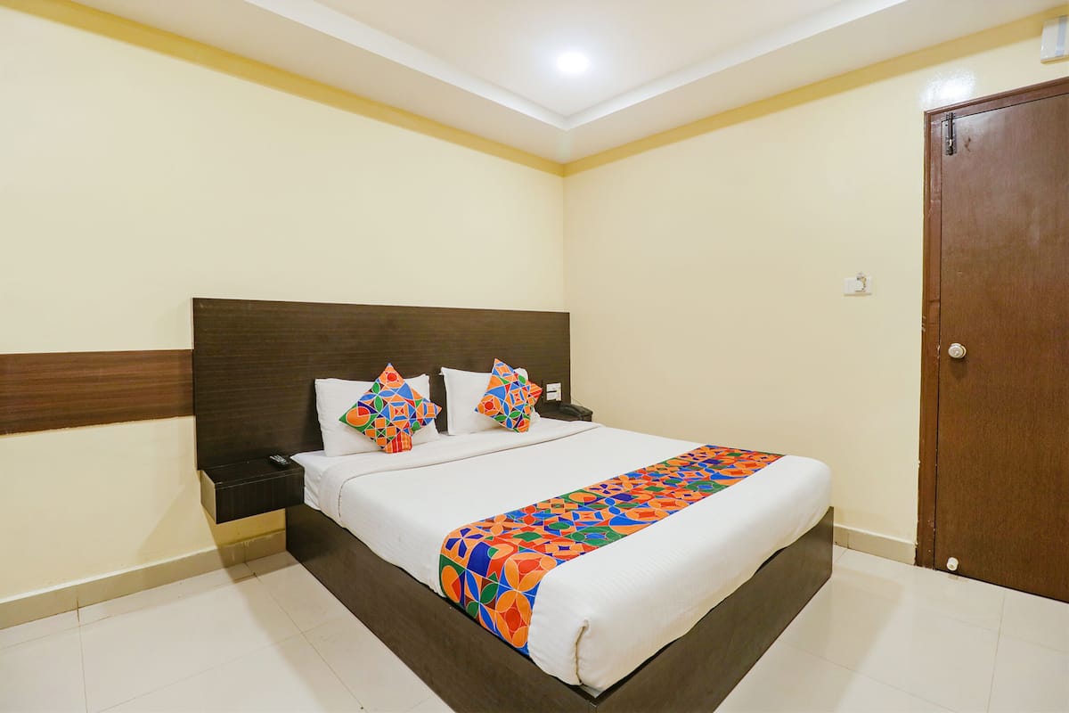 Cama bem arrumada com um cobertor colorido, cabeceira de madeira e mesa de cabeceira com um telefone.