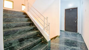A staircase with marble steps and a white handrail, leading to a door with a number plate. - FabExpress Wakad Stays (Paud)
