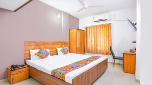 A bedroom with a wooden bed, a nightstand with a phone, a desk, and a chair. - FabExpress Wakad Stays (Paud)