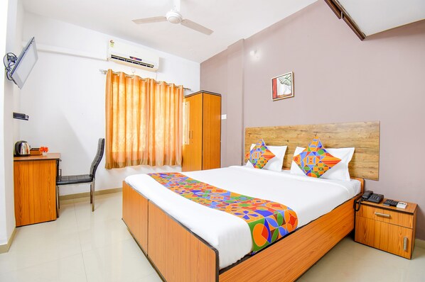 A neatly arranged bedroom with a bed, bedside table, nightstand, and a desk with a chair. - FabExpress Wakad Stays (Paud)