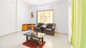 A living room with a glass coffee table, two leather sofas, a wooden cabinet, and a ceiling fan. - FabExpress Wakad Stays (Paud)