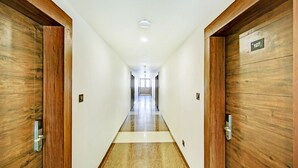 Um corredor comprido e estreito com portas de madeira em ambos os lados, piso de mármore e uma placa indicando a sala 107.