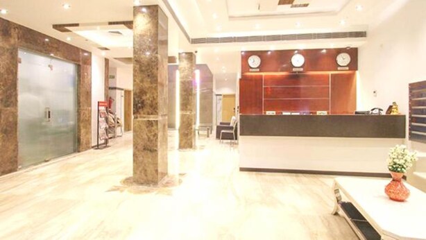 Uma área de recepção de hotel com piso de mármore, um balcão de atendimento e um relógio na parede.