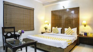 Quarto de hotel bem arrumado, com cama, mesas de cabeceira, uma cadeira e uma pequena mesa com um vaso de flores.