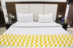 A hotel room with a large bed, two white pillows, a nightstand with a phone and a book, and a vase with flowers on the left side. - FabHotel Station 3 (New Delhi)