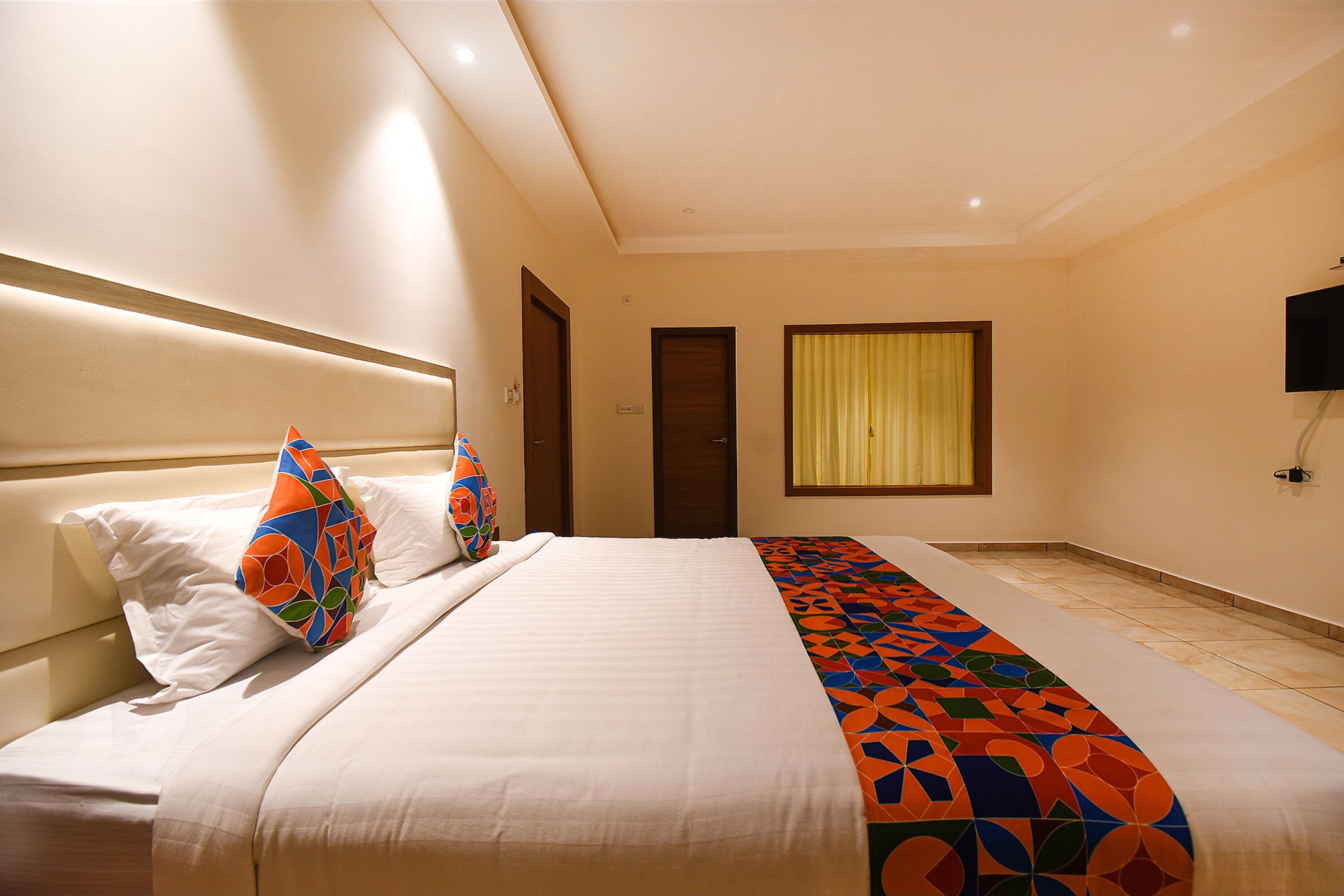 A hotel room with a bed, a TV, and a window with curtains.