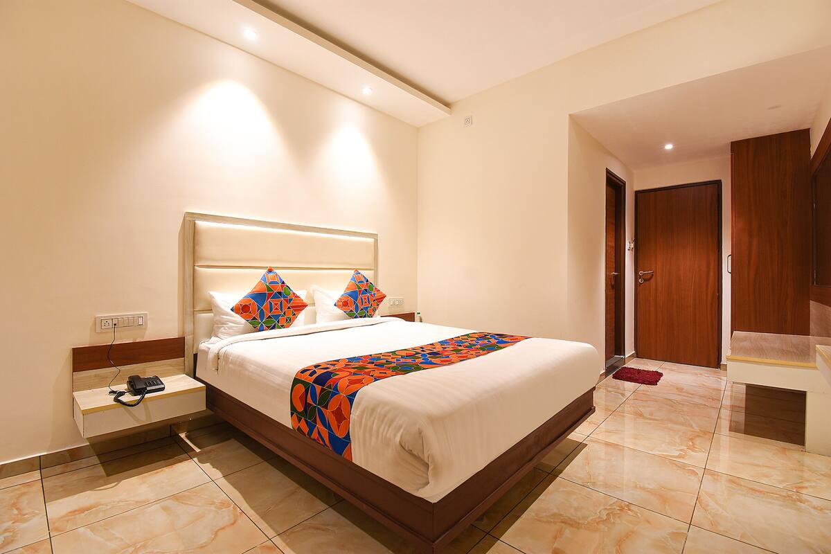 Quarto de hotel com uma cama grande, mesa de cabeceira, guarda-roupa de madeira e um banheiro visível por uma porta aberta.