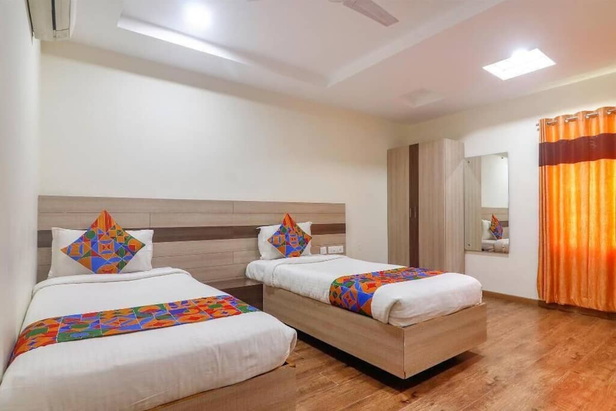 A hotel room with two beds, a wooden headboard, a mirror, and an orange curtain.
