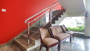 A staircase with a red wall, a glass railing, and two upholstered chairs at the bottom. - Fabhotel Pride Inn Financia (Hyderabad)